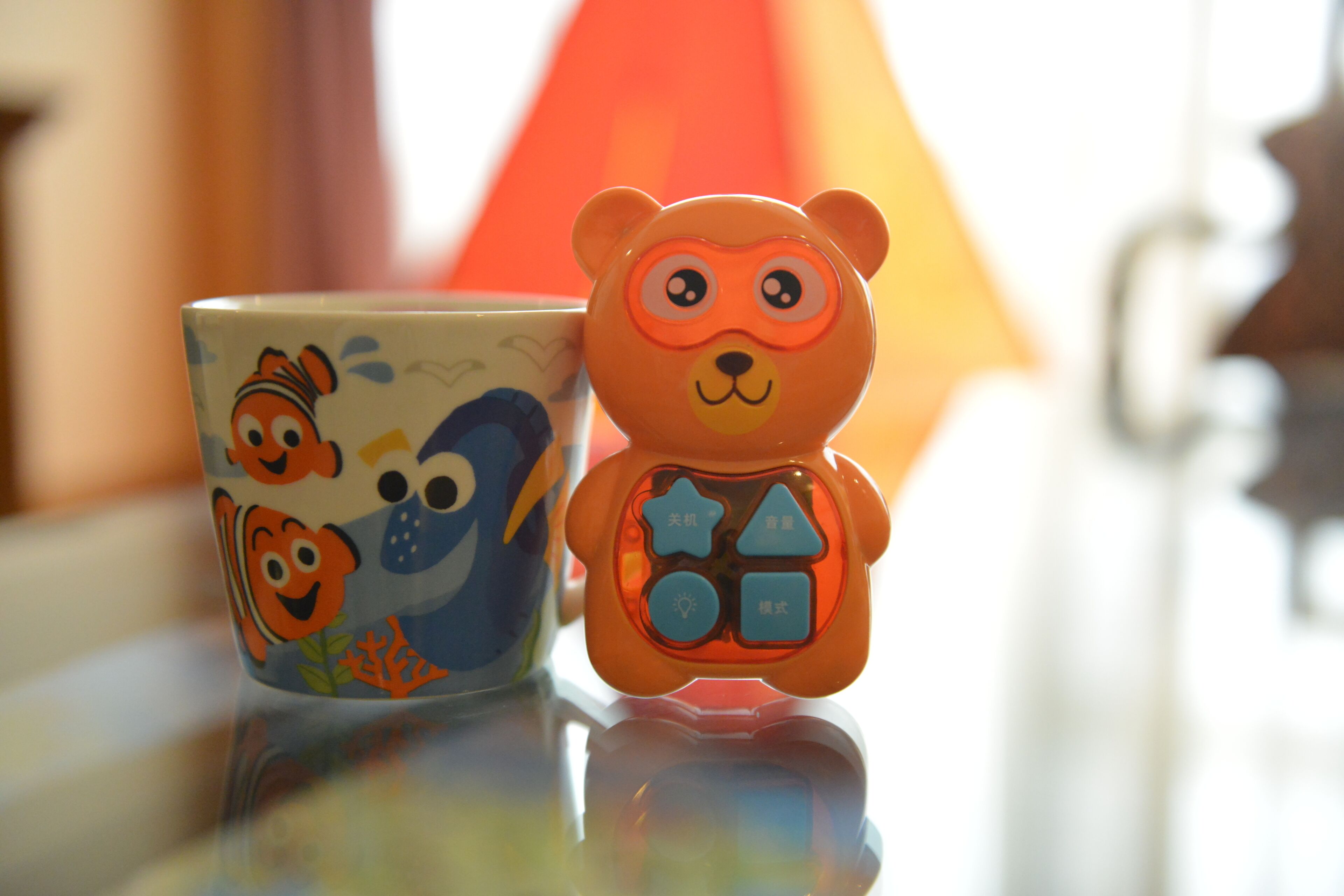 A ceramic mug with a fish design and a bear-shaped toy with buttons.