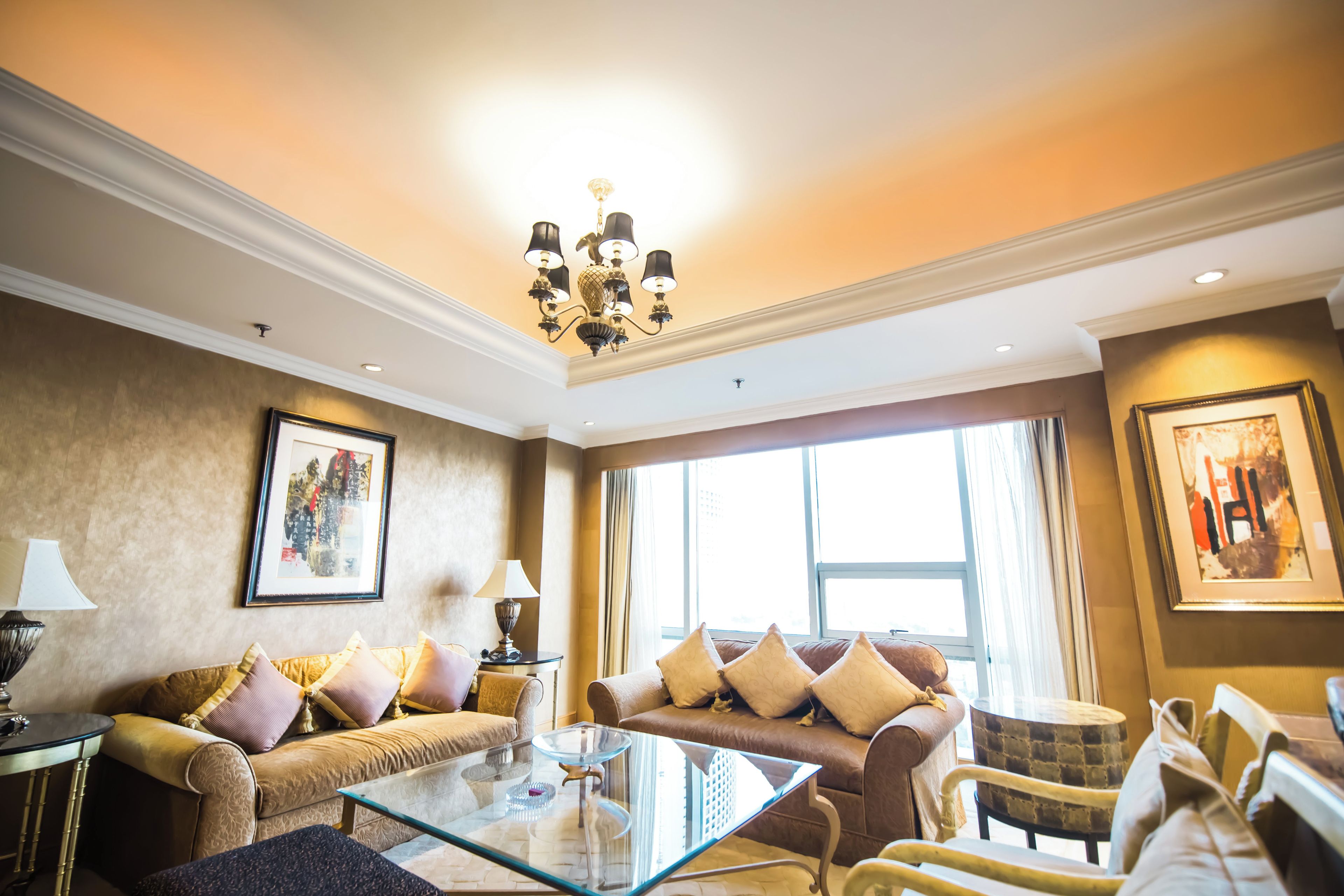 A well-lit living room with a glass coffee table, leather sofas, and a chandelier.