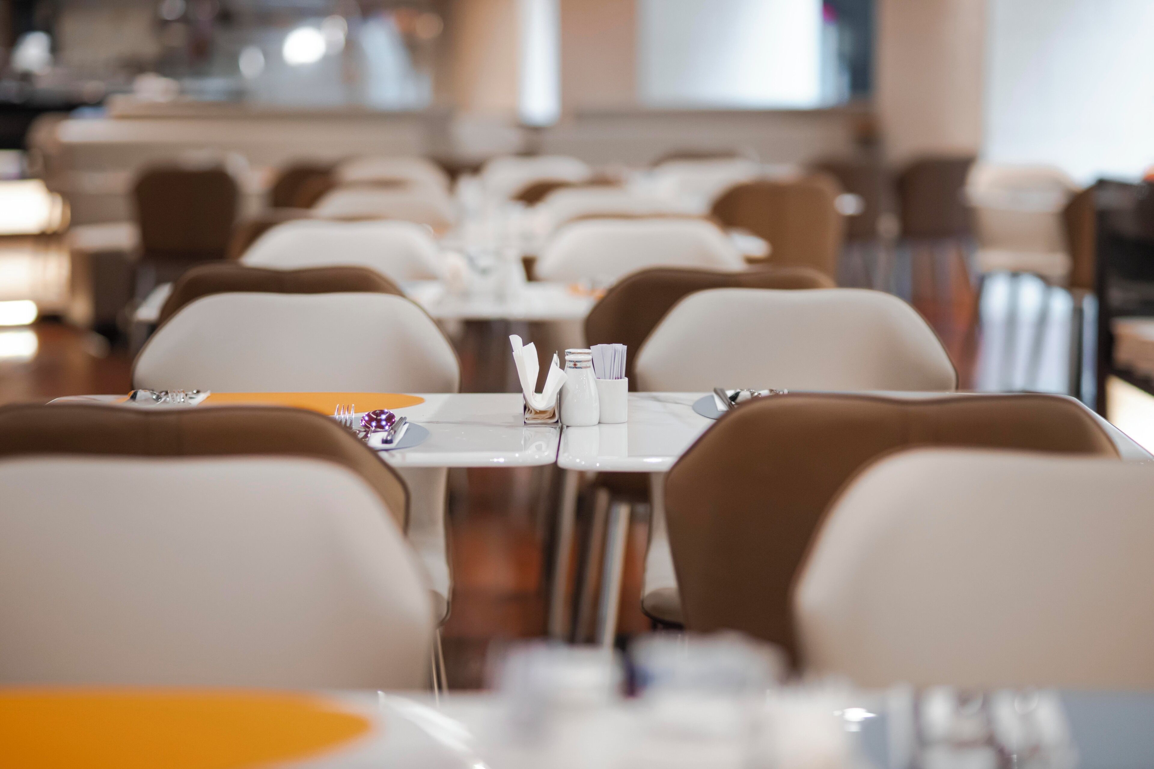 A restaurant with rows of tables and chairs, each set with a menu, napkin, and glass.