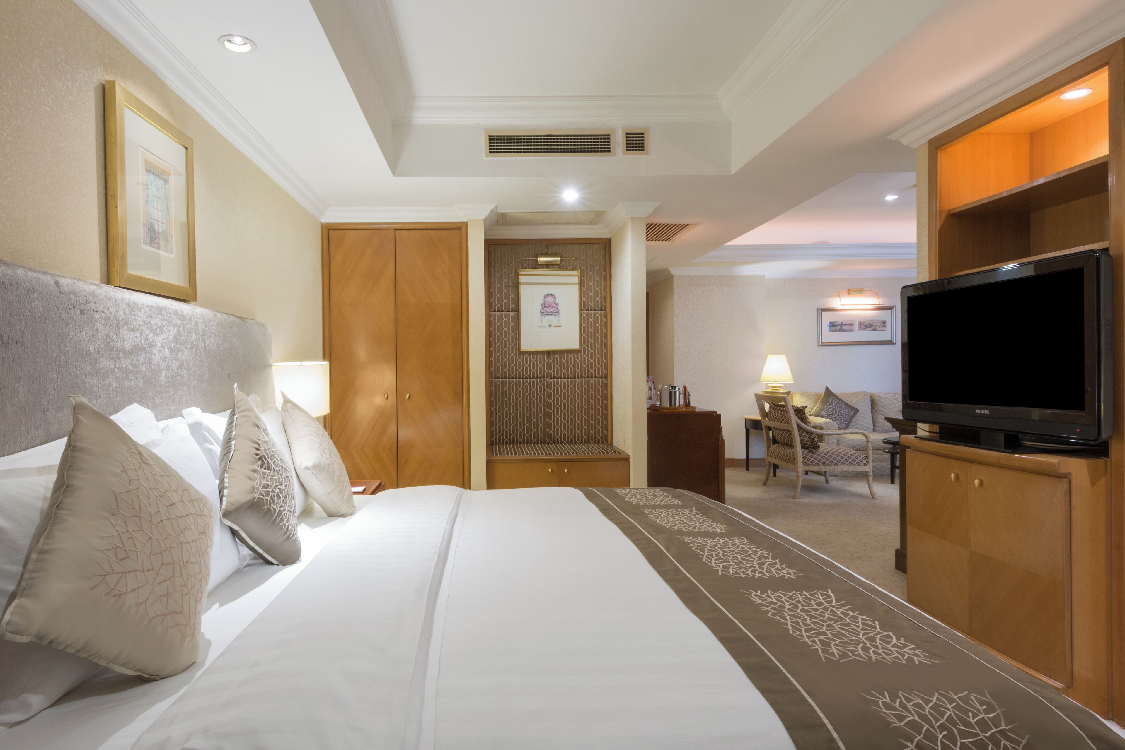 A hotel room with a large bed, a television, a desk with a lamp, and a chair.