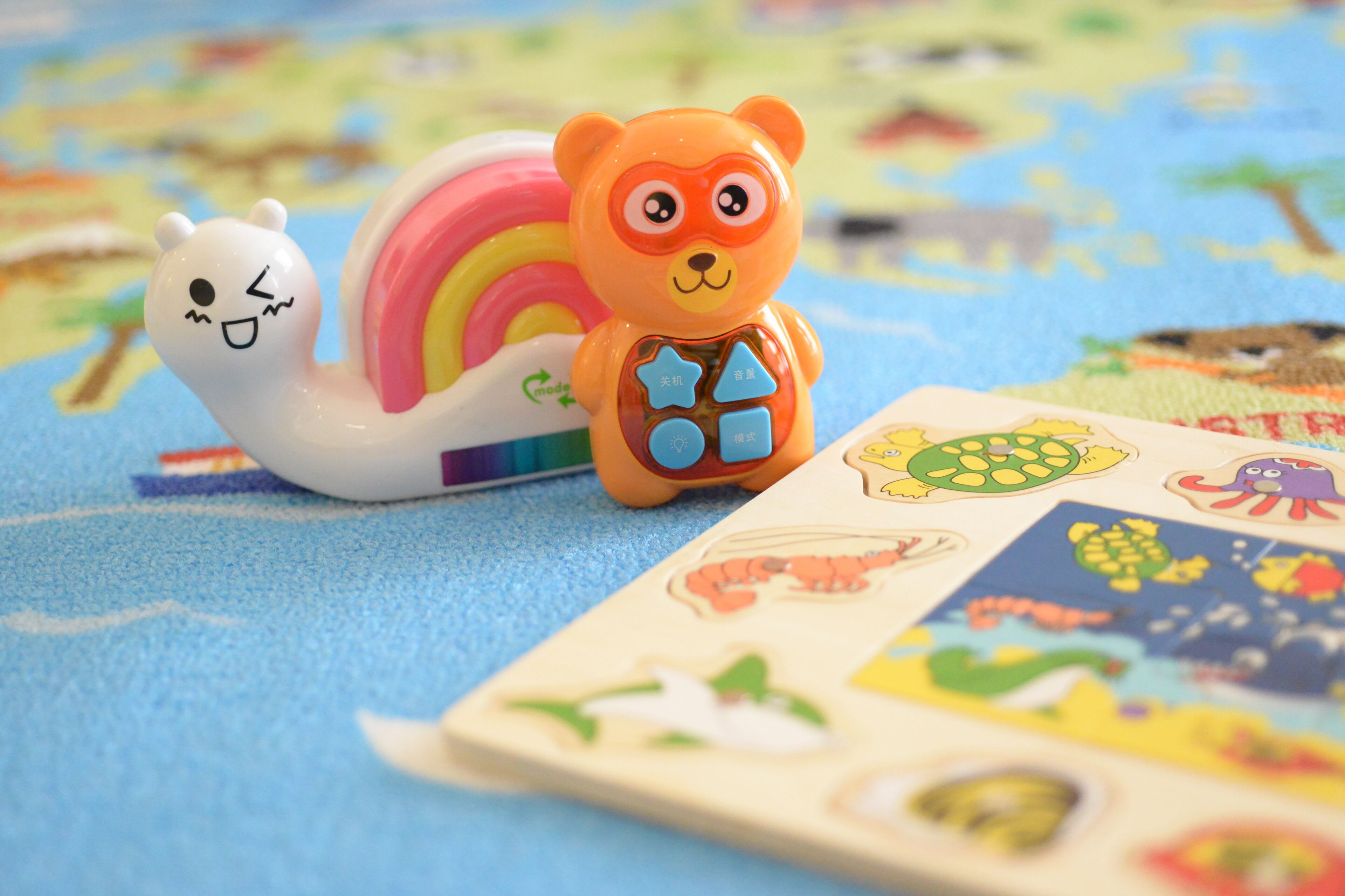 A toy snail and bear on a colorful play mat with various animal illustrations.