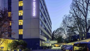 A modern hotel building with illuminated signage, a parking area, and a well-maintained garden. - Mercure Hotel Köln Belfortstraße (Cologne)