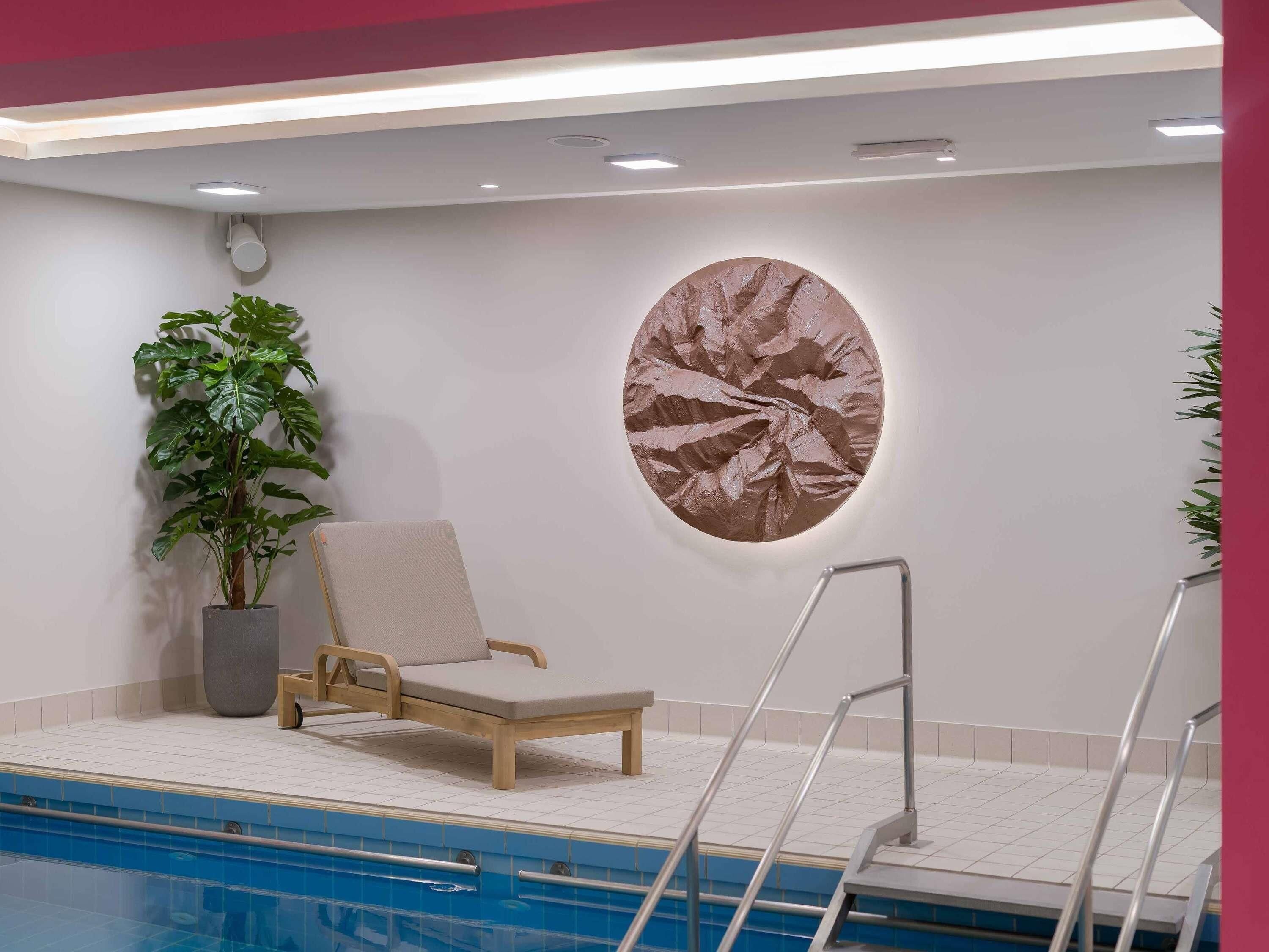 A pool area with a lounge chair, a potted plant, and a wall-mounted artwork.