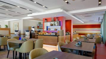 A modern restaurant with multiple dining tables and chairs, a bar area, and a kitchen in the background.