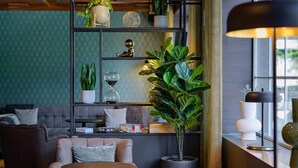 A modern living room with a sofa, two round tables, a bookshelf with plants, and a window with a lamp. - Mercure Hotel Köln Belfortstraße (Cologne)