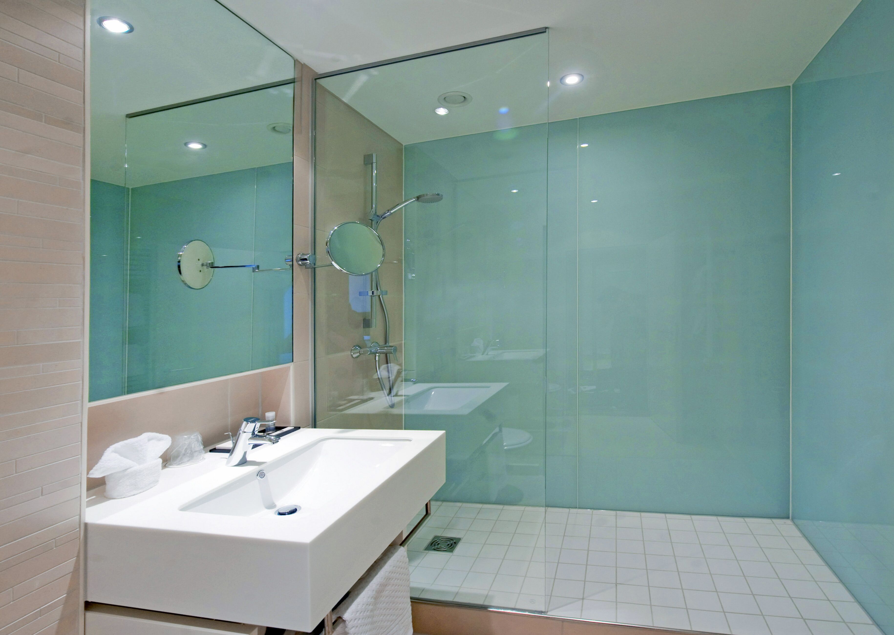 A modern bathroom with a large mirror, a white sink, and a glass-enclosed shower area.