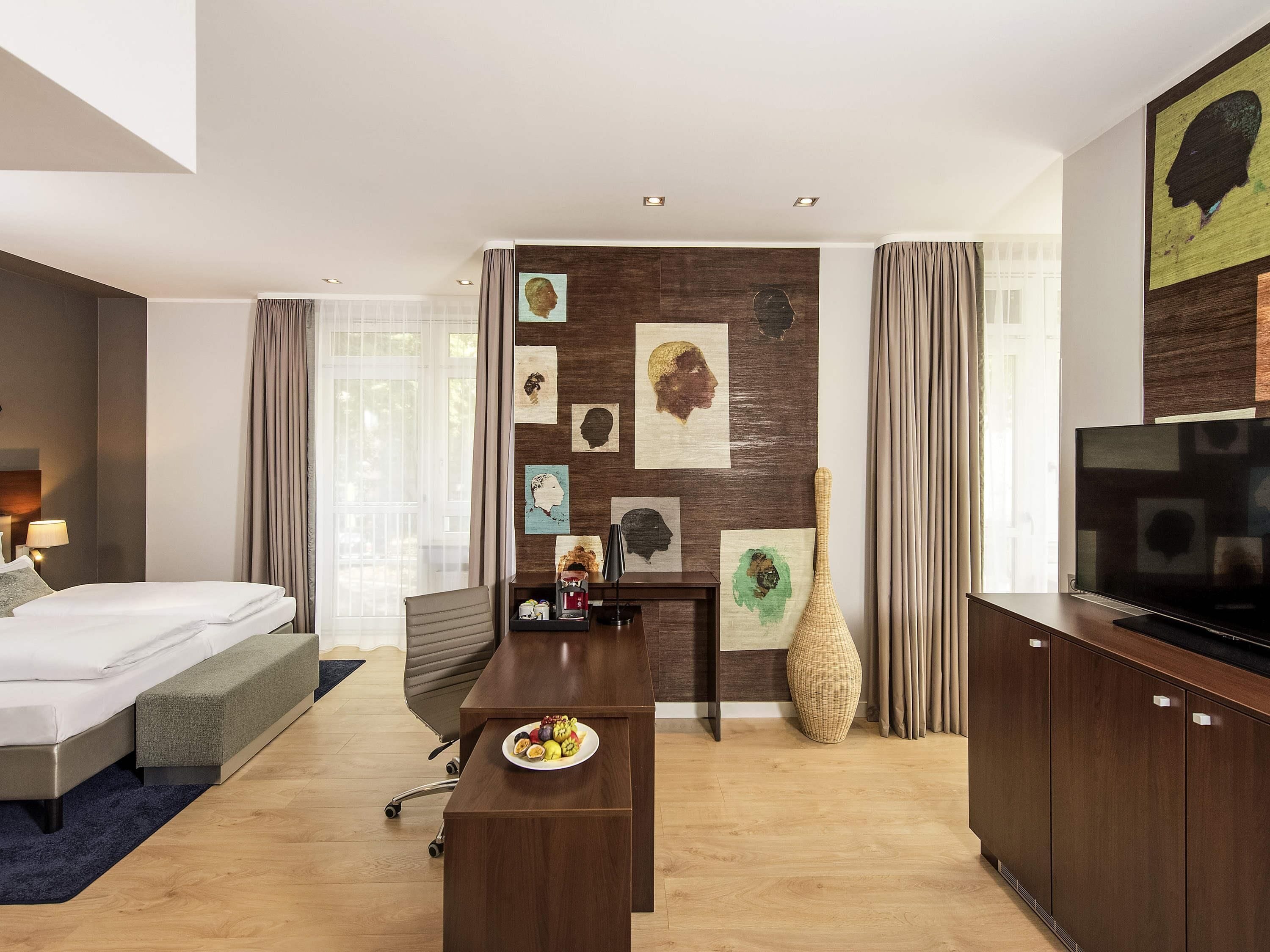 Ein modernes Hotelzimmer mit Bett, Schreibtisch, Fernseher, Wandbild und einem großen Fenster.