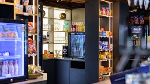 A modern bar area with shelves stocked with snacks, a refrigerator with beverages, and a counter with a digital display. - Mercure Hotel Köln Belfortstraße (Cologne)
