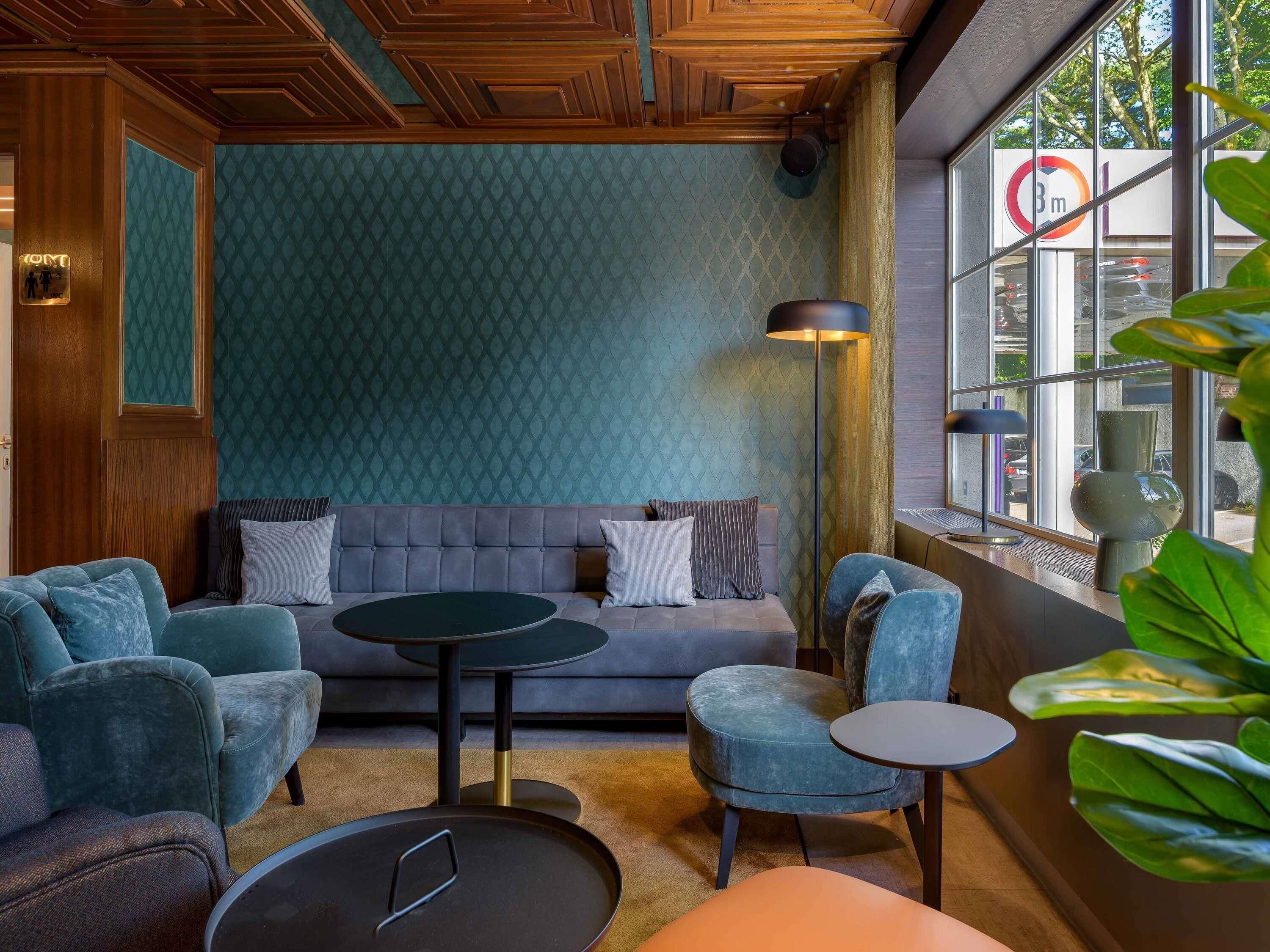 Een kamer met een bank, twee fauteuils, een kleine tafel, een vloerlamp en een groot raam met uitzicht op de straat.
