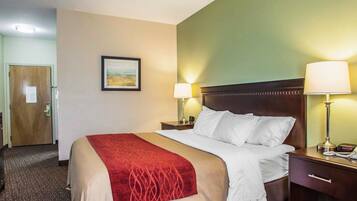 A hotel room with a bed, two bedside tables with lamps, a door, a framed picture on the wall, and a carpeted floor.