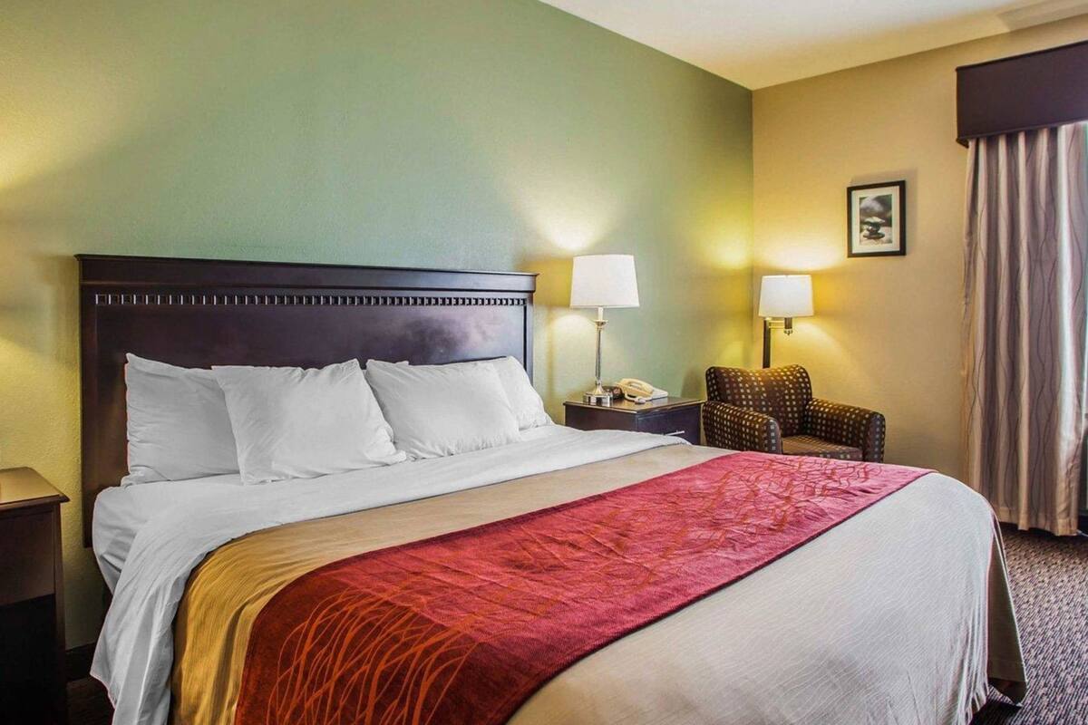 Una habitación de hotel con una cama grande, dos mesitas de noche, una silla y una lámpara.