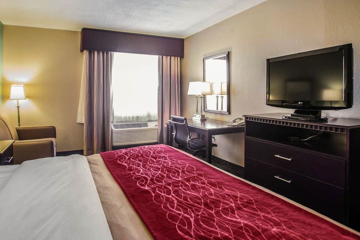 Una habitación de hotel con una cama, un escritorio con una silla, un televisor y una lámpara.