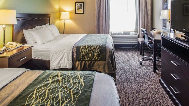 Een hotelkamer met twee bedden, een bureau met een lamp, een televisie en een airconditioner.