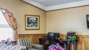 Een hotel lobby met gestreepte banken, een houten bureau met een computer en een lijst met een landschapsgezicht aan de muur.