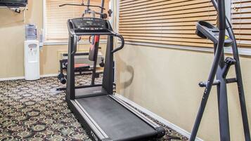 Habitación de hotel con cinta de correr, dispensador de agua y televisor.