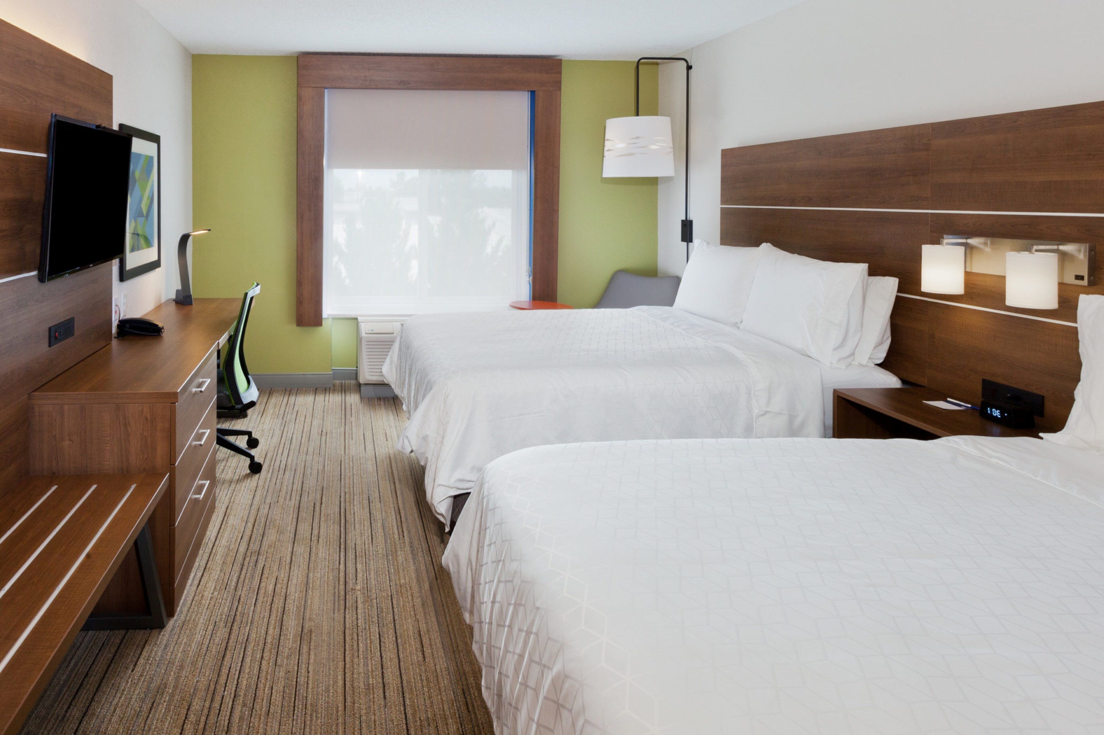 Ein Hotelzimmer mit zwei Betten, einem Fernseher, einem Schreibtisch und einem Fenster mit Jalousien.