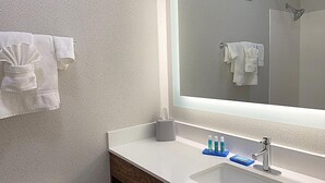 A modern bathroom with a large mirror, white towels, a sink, and toiletries.