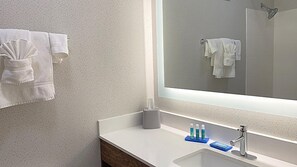 A modern bathroom with a large mirror, white towels, a sink, and toiletries.