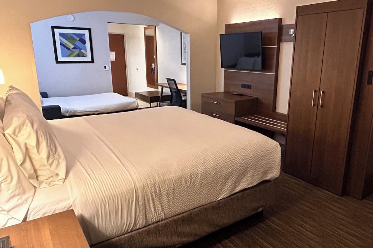 A hotel room with a large bed, a desk, a chair, a TV, and a wardrobe.