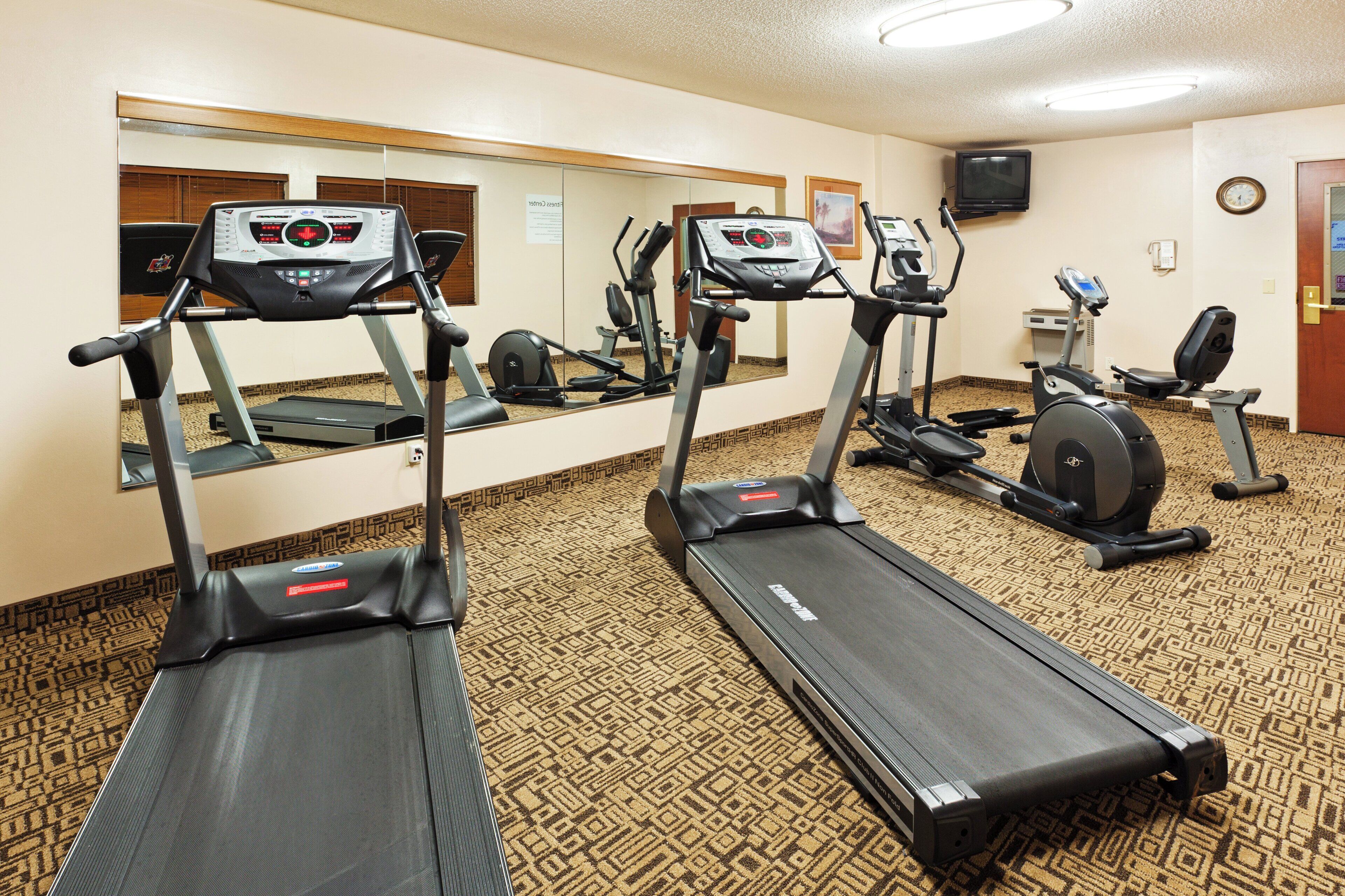 A hotel fitness center with treadmills, a stationary bike, and a mirrored wall.