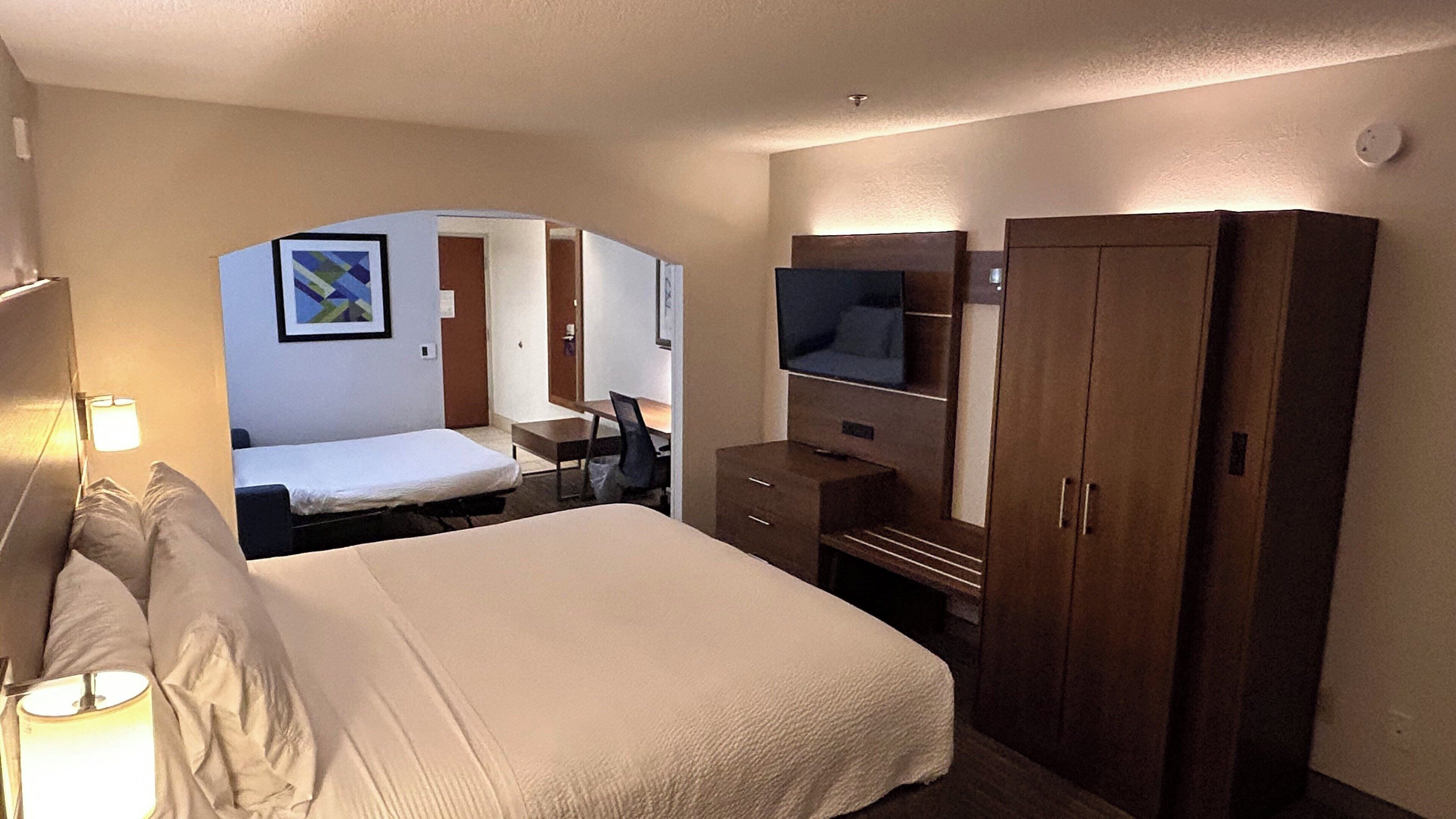 A hotel room with a bed, a desk, a chair, a television, and a wardrobe.