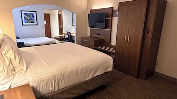 Habitación de hotel con una cama grande, un escritorio, una silla, un televisor y un armario.