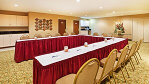 A conference room with a long table, chairs, a kitchen area, and a decorative wall.