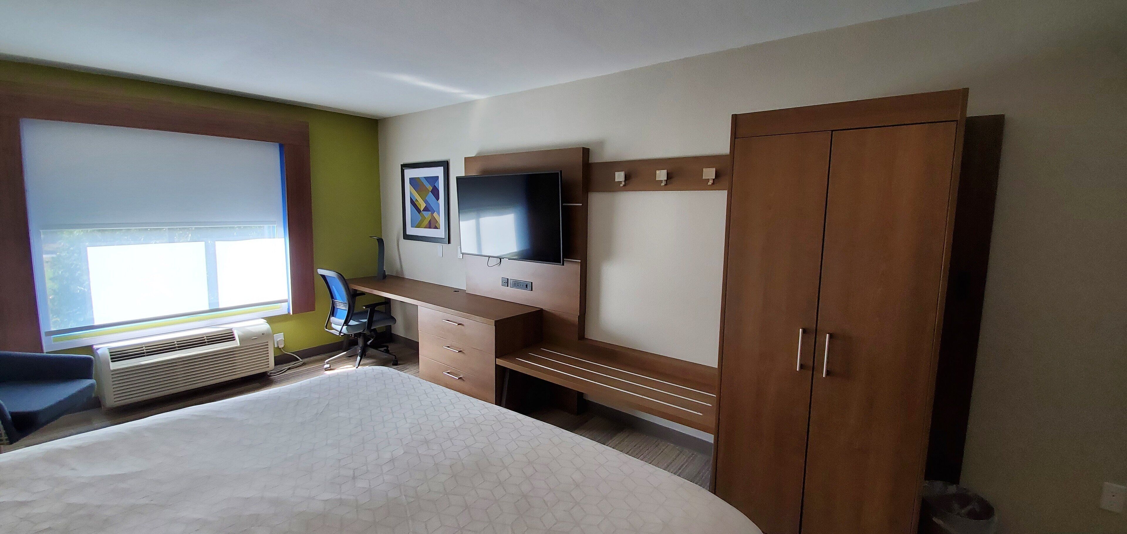 A hotel room with a bed, a desk with a chair, a TV, and a wardrobe.