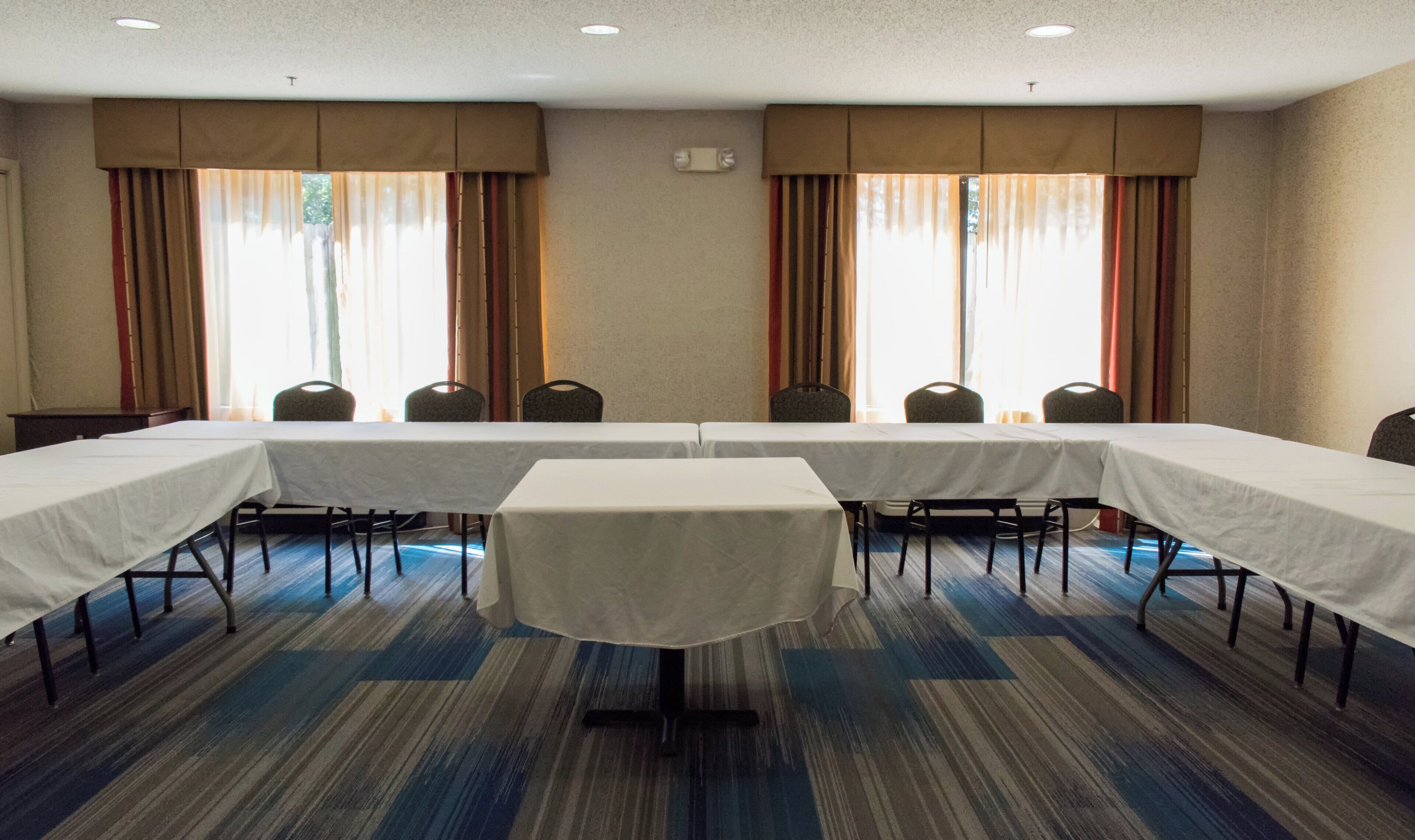 A conference room with a long table, chairs, and large windows with curtains.