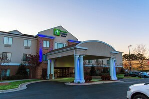 A Holiday Inn Express & Suites building with a covered entrance, a parking lot, and a clear sky.