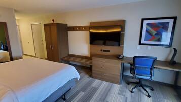 A hotel room with a bed, a desk with a chair, a wardrobe, and a TV.
