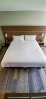 Una cama bien tendida con sábanas blancas, un cabecero de madera y dos mesitas de noche con lámparas y un teléfono.