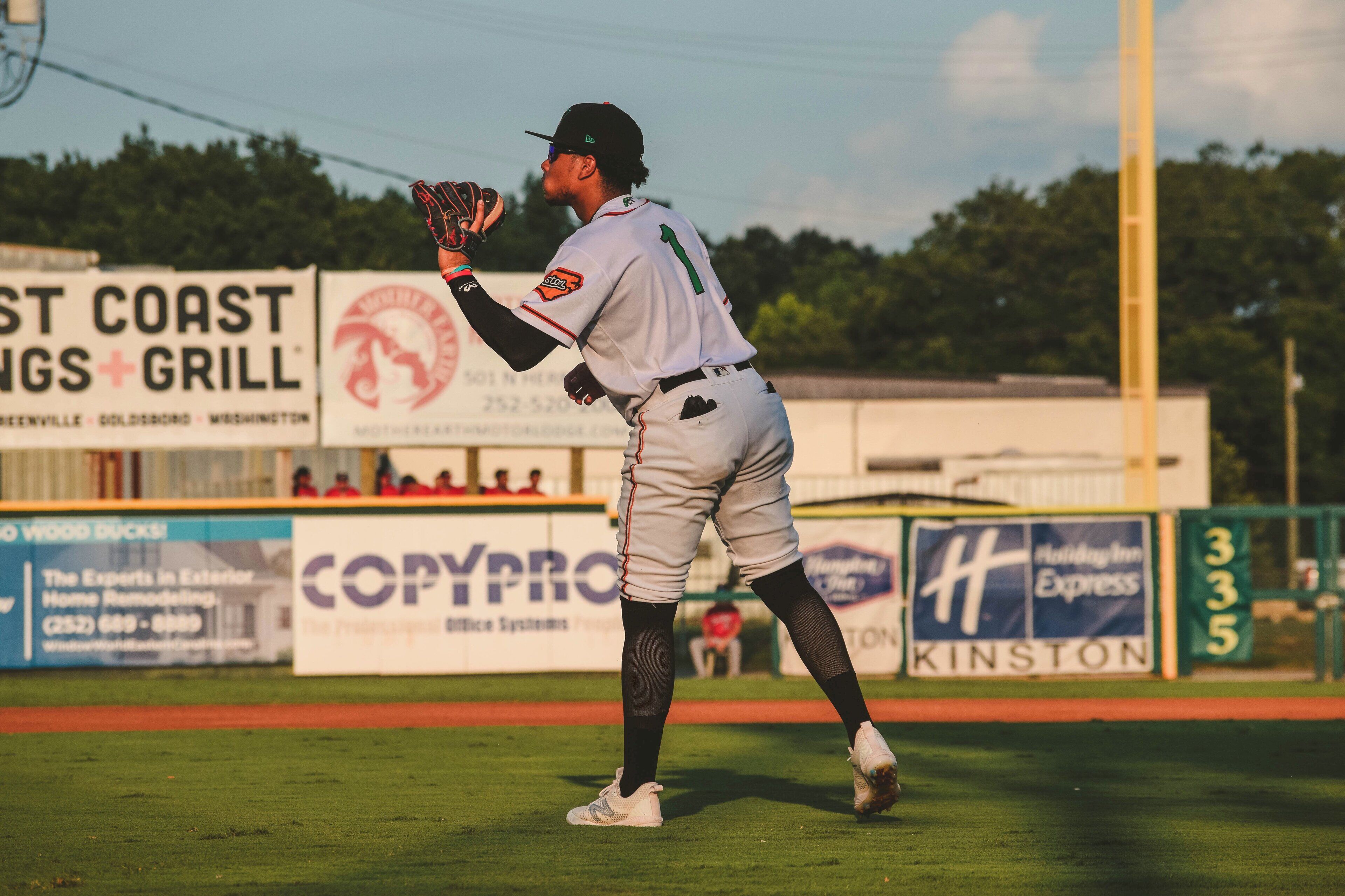 A baseball player in a white uniform with the number 1, standing on a field with advertisements in the background.