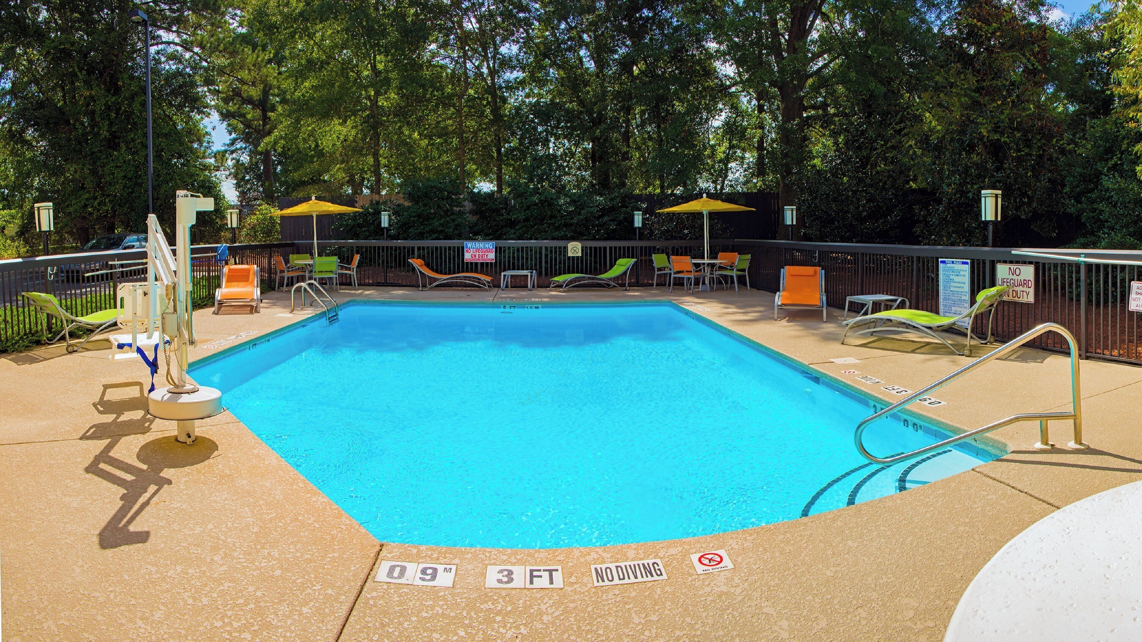 A rectangular pool with a diving board, surrounded by lounge chairs and umbrellas.