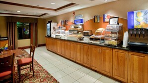 Un área de desayuno de hotel con un mostrador de buffet, una máquina de café y un dispensador de zumo.