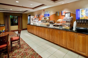 A hotel breakfast area with a buffet counter, a coffee machine, and a juice dispenser.