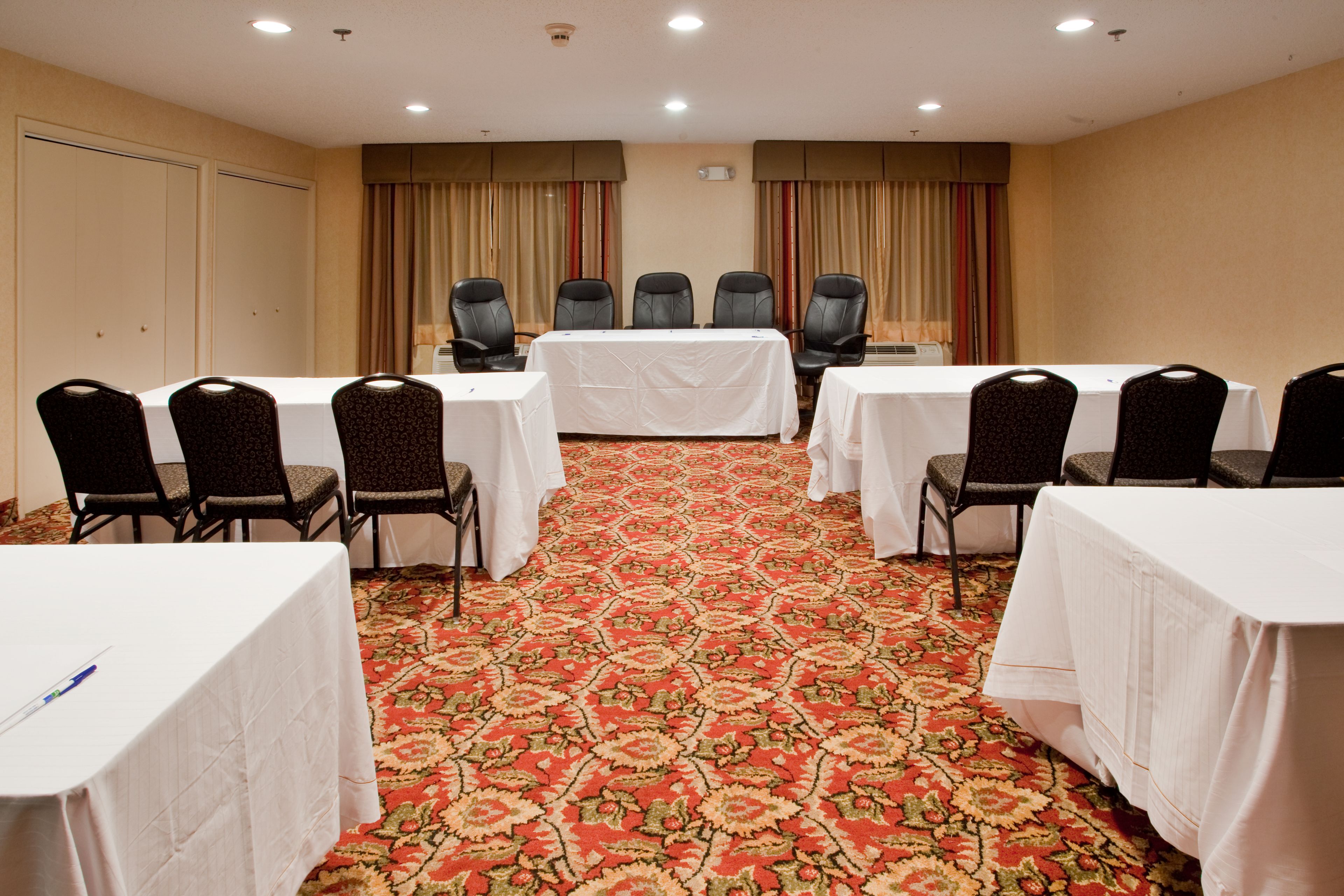 A conference room with a carpeted floor, white tables, and black chairs.