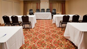 Un salón de conferencias con piso alfombrado, mesas blancas y sillas negras.