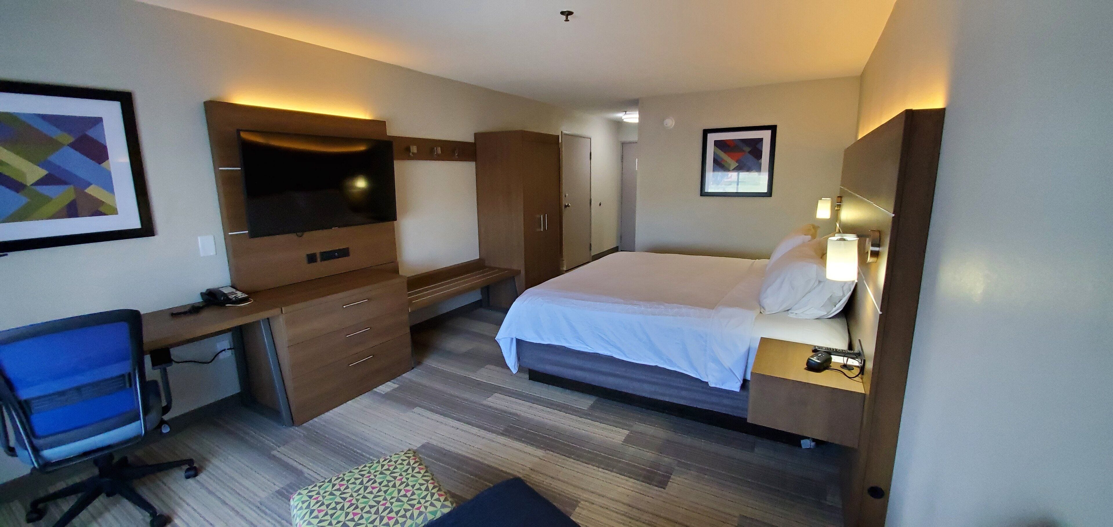 A hotel room with a bed, desk, chair, and a television.
