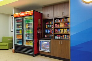 Un'area con distributori automatici, tra cui un refrigeratore per Coca-Cola, un frigorifero più piccolo e scaffali pieni di snack e bevande.