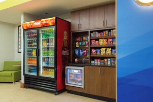 Un área de venta con un refrigerador de Coca-Cola, un refrigerador más pequeño y estantes llenos de aperitivos y bebidas.