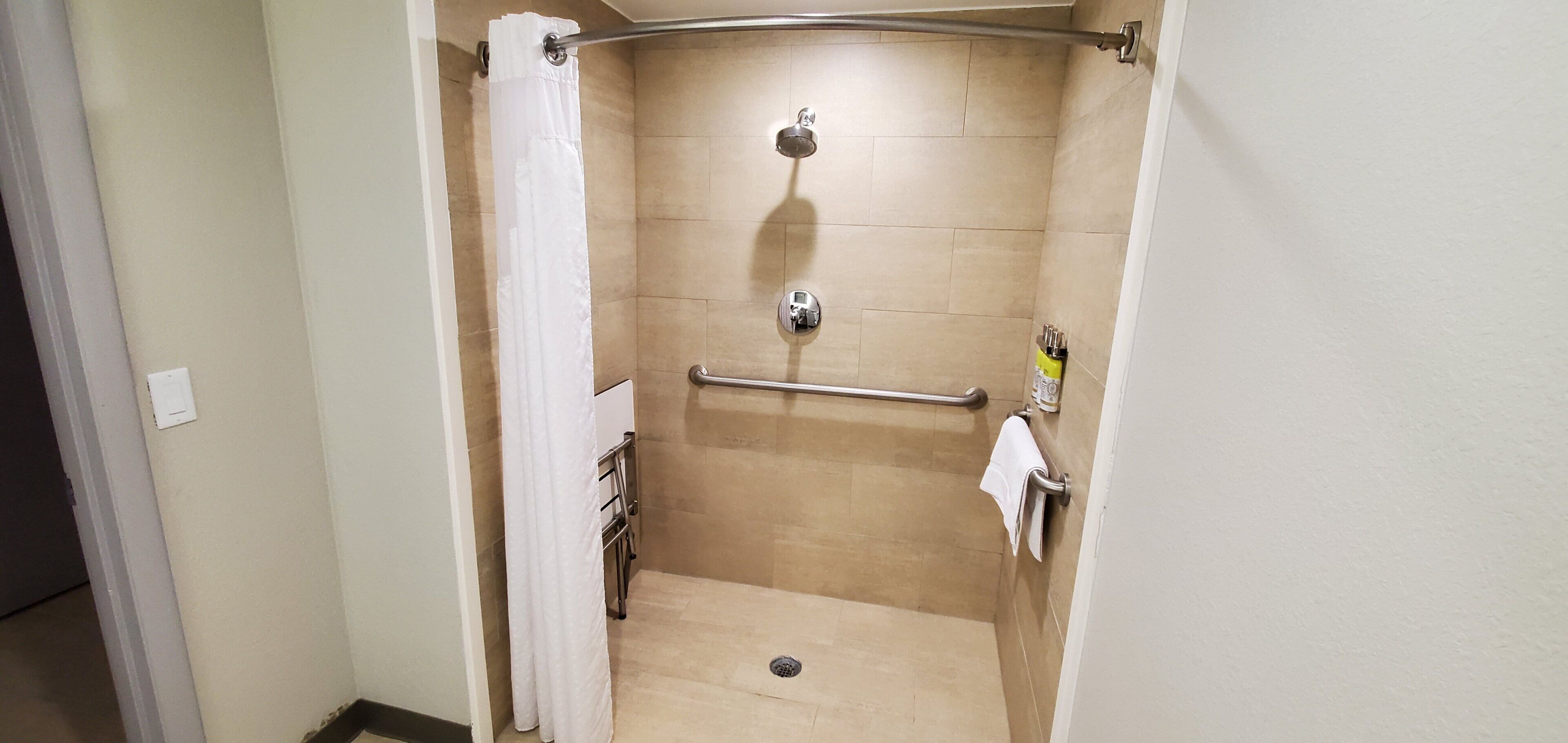 Un espacio de ducha pequeño y cerrado, con una barra de apoyo, un perchero y un cabezal de ducha.