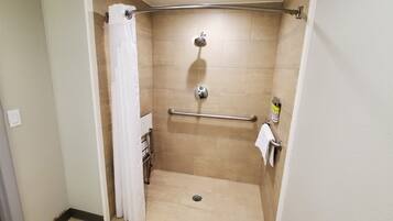 Un espacio de ducha pequeño y cerrado, con una barra de apoyo, un perchero y un cabezal de ducha.