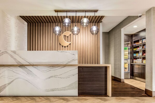 Un mostrador de recepción con diseño de mármol, un panel de listones de madera y una decoración con forma de luna creciente.