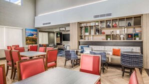 A modern dining area with red and blue chairs, a wooden table, and a sofa with patterned ottomans.