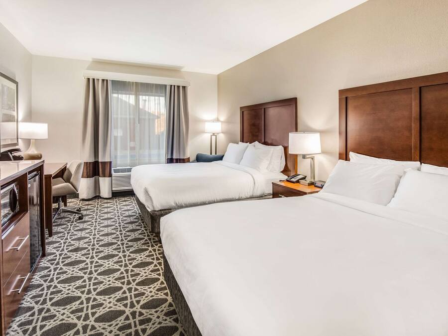 A hotel room with two beds, a desk, a chair, a TV, and a patterned rug.