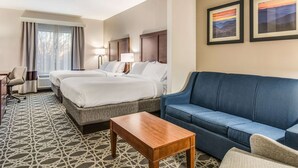 A hotel room with two beds, a blue sofa, a wooden coffee table, and a patterned carpet.