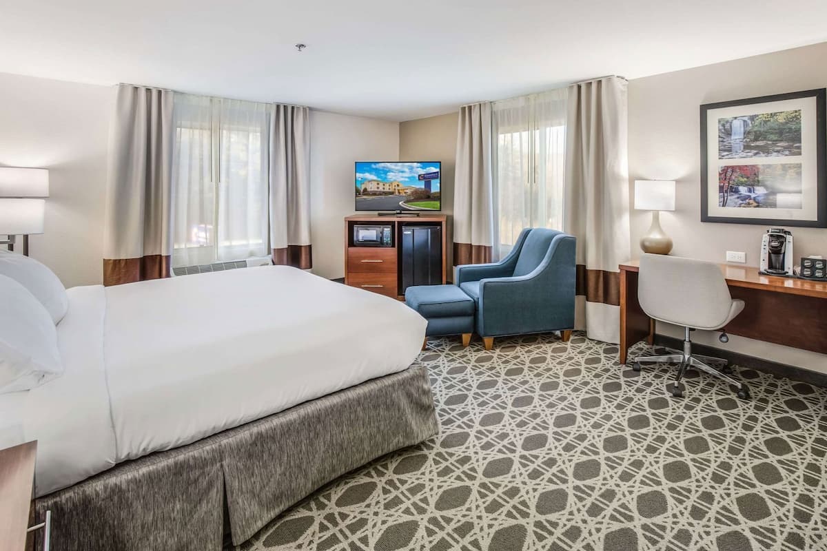A hotel room with a large bed, a desk, a chair, a TV, and a coffee maker.