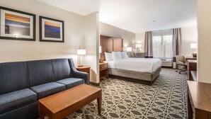 A hotel room with a bed, a sofa, a desk, and two framed pictures on the wall.