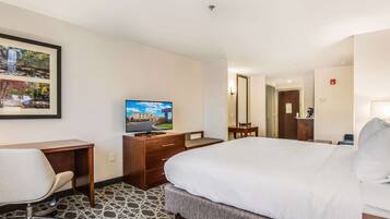 A hotel room with a bed, a desk with a chair, a television, and a framed picture on the wall.